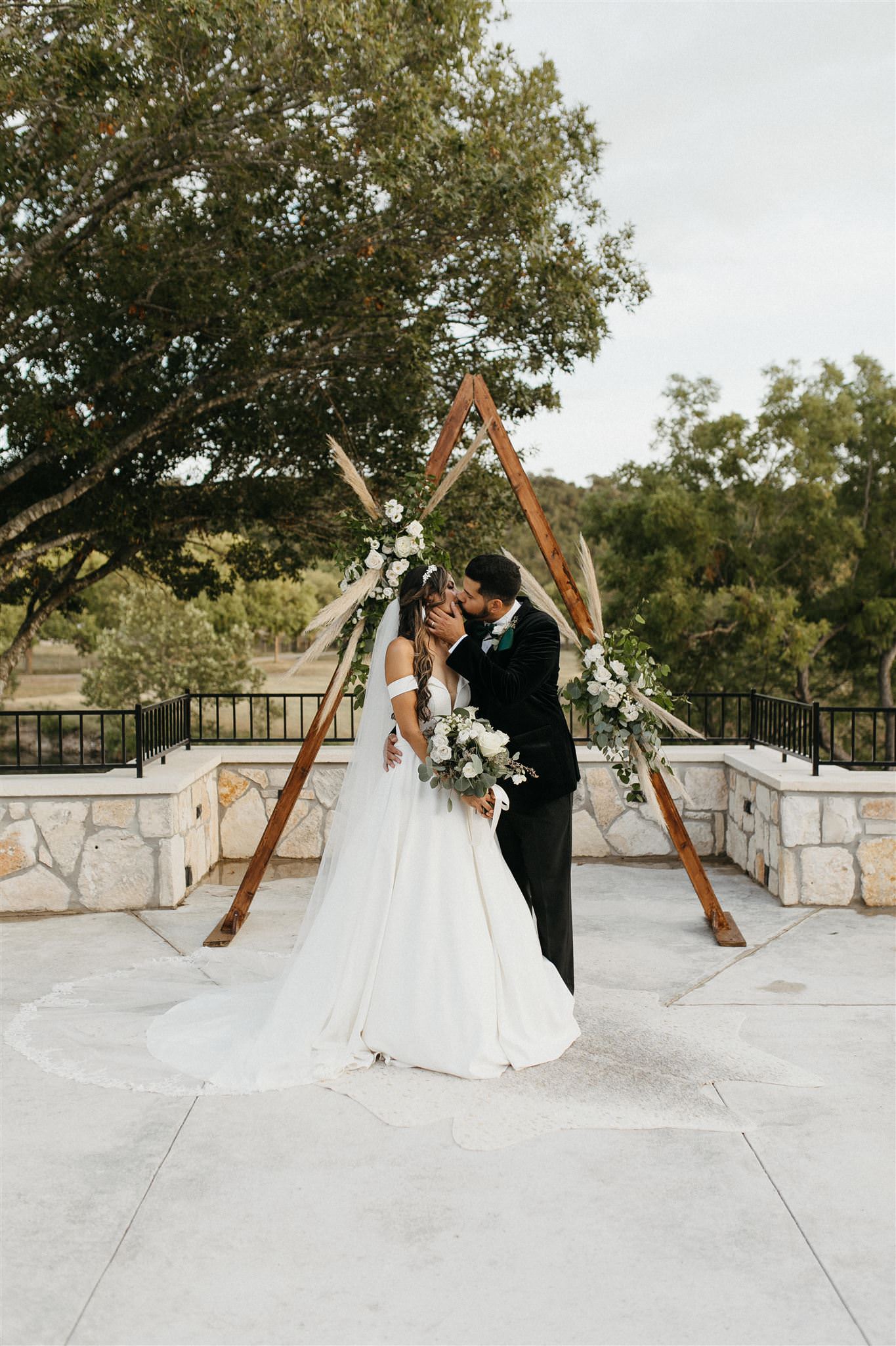 bride and groom kissing at ceremony site with triangle arch and boho vibes kerrville photographer Leah thomason