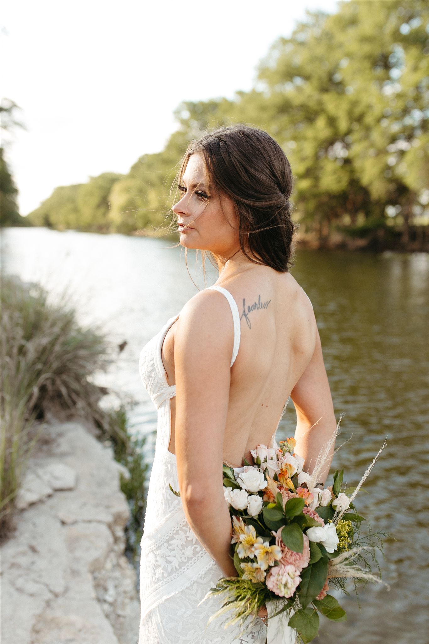 bride looking down river holding flowers. San Antonio wedding photographer Leah Thomason.