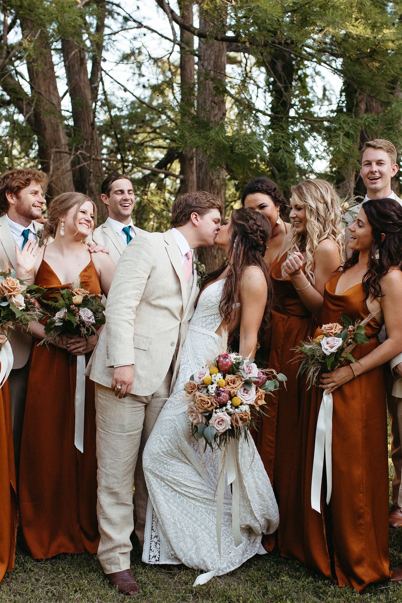 rust and neutral wedding party with bride and groom kissing