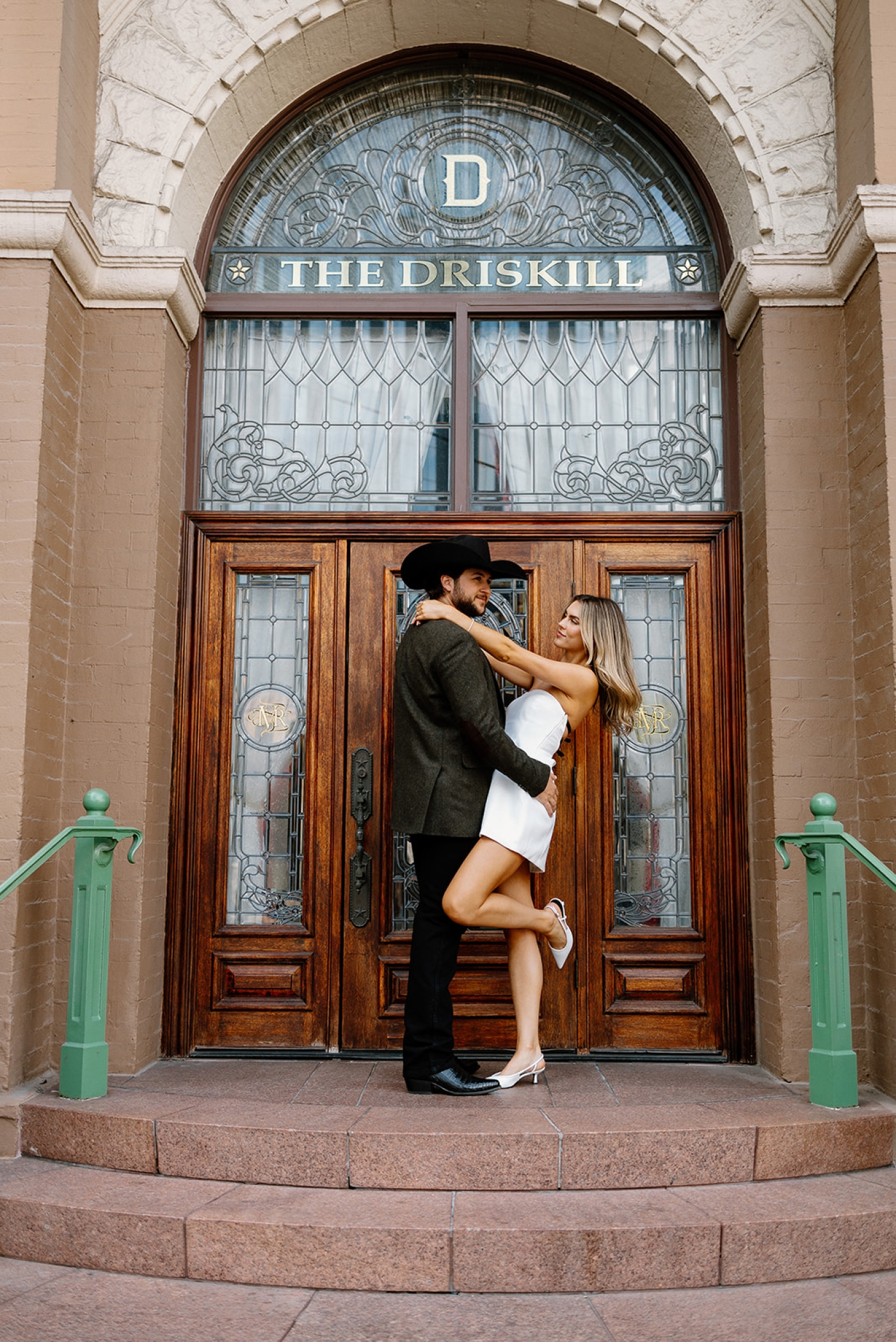 A man and woman pose outside the stained glass and wood door of the Driskill Hotel